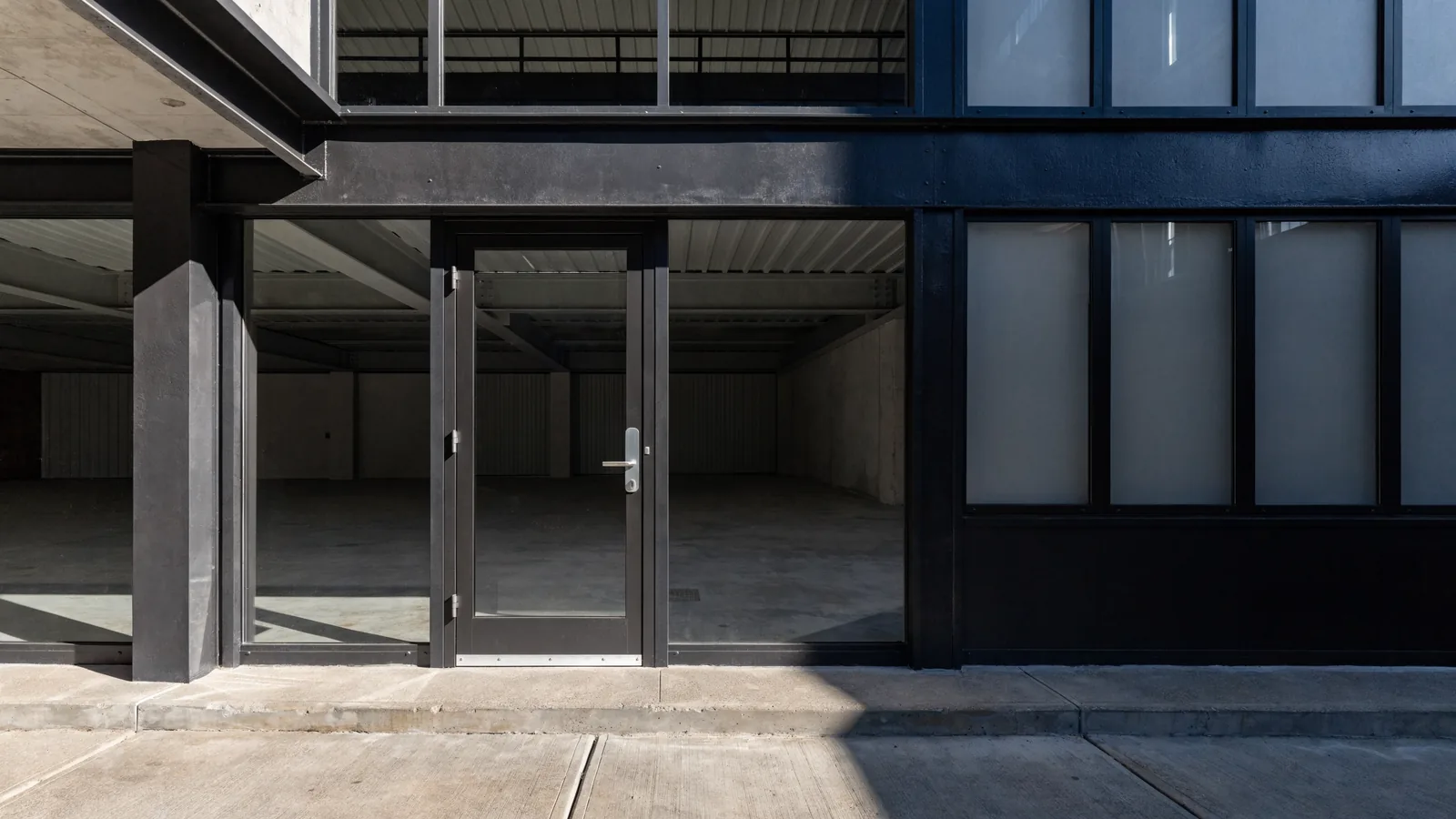 The entrance to a newly finished industrial tenant suite: a plain glass door in a painted storefront frame, fresh paint and a clean concrete walkway.