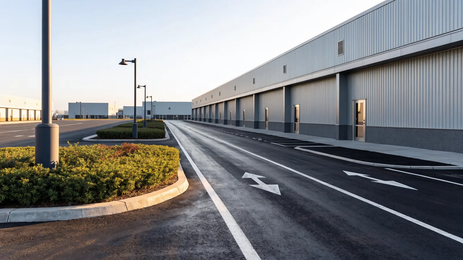The shared drive of a multi-tenant industrial park, freshly resurfaced and striped, with kerbed landscape islands, light poles and a row of tenant doors.